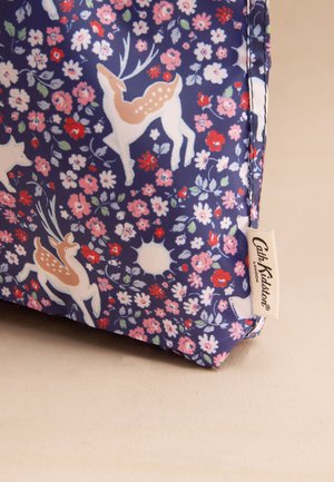 Laivastonsininen kangaslaukku, jossa kukka- ja peura-aihe; siinä on vaaleanpunaisia ja valkoisia kukkia, yksityiskohtainen peura sekä sivussa pieni merkkitunniste.