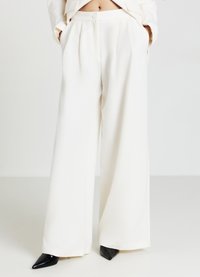 Pantaloni a gamba larga in tessuto bianco, con vita alta, pieghe, tasche laterali e tacchi a punta neri. Tessuto morbido e vestibilità su misura.