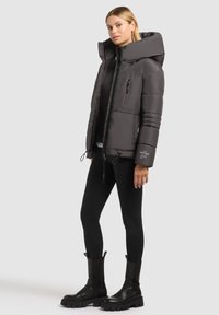 Grå puffjacka med hög krage, dragkedja och detaljer på framfickorna. Matchad med svarta leggings och kraftiga svarta stövlar.