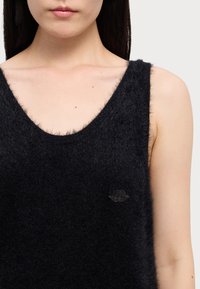 Black sleeveless knit top with a deep V-neck, made of soft, fuzzy material. Features a small, dark logo on the left side near the chest.