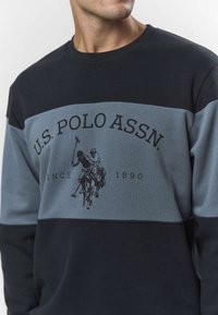 Fekete és szürke pamut pulóver középen lovas póló játékosokat ábrázoló logóval, kerek nyakkivágással és kontrasztos vízszintes színblokkokkal.