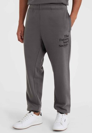 Gray sweatpants with an elastic waistband, side pockets, and printed text "The Future Surf Society" in black. Paired with white sneakers.