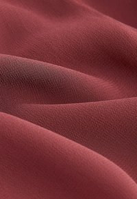 Tessuto in un profondo tono di rosso, caratterizzato da una morbida e liscia texture con un leggero stretch, che si drappeggia elegantemente in onde e pieghe dolci.