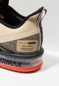 Sneaker Nike Run Utility en beige et marine avec un tissu texturé, des détails réfléchissants et un amorti à air. Présente un design résistant à l'eau.