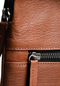Braune Ledertasche mit strukturiertem Oberflächenmaterial, einem Reißverschluss und sichtbaren Nähten. Das Design umfasst mehrere Fächer für Funktionalität.