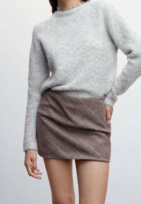 Suéter gris difuso de manga larga y escote redondo combinado con una mini falda ajustada de cuadros marrones con acentos rojos y azules.