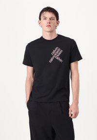 Zwarte katoenen t-shirt met diagonale witte en roze "calvin klein" tekst. Korte mouwen, ronde hals, relaxte pasvorm, gladde textuur.