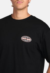 Sort bomulds t-shirt med et rundt logo i pink og hvid på venstre bryst, korte ærmer og et klassisk crew neck-design.
