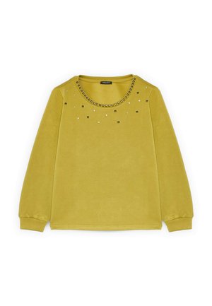 Żółta bluzka z długim rękawem, z okrągłym dekoltem, ozdobiona metalowymi ćwiekami wokół kołnierza oraz rozproszonymi detalami z przodu.