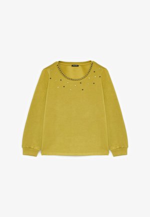 Żółta bluzka z długim rękawem, z okrągłym dekoltem, ozdobiona metalowymi ćwiekami wokół kołnierza oraz rozproszonymi detalami z przodu.