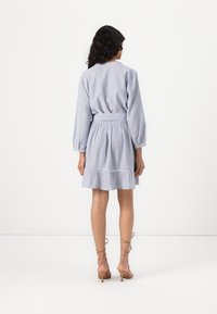 Abito a righe blu e bianche con un corpetto aderente, maniche a sbuffo, vita elastica e orlo a strati con volant. Indossato con sandali beige con fasce.