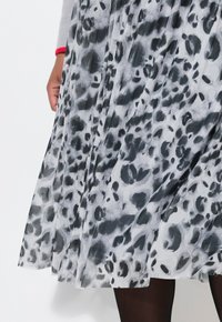 Abito plissettato caratterizzato da un tessuto traslucido con un design astratto di stampa leopardata in nero e grigio, abbinato a collant neri.
