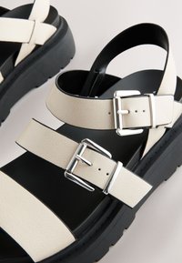 Beige leren platform sandalen met twee verstelbare bandjes, zilverkleurige metalen gespen en een dikke zwarte rubberen zool.