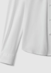 Vit skjorta med lång ärm, slät tyg, rundad nederkant och smala manschetter. Har enkla knappar och en ren, professionell design.