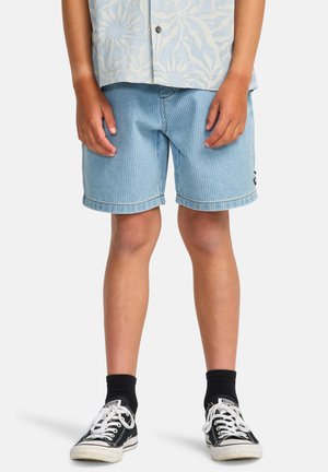 Pantaloni scurți bleu deschis din catifea cu tiv pliat, asortați cu teniși negri și șosete închise la culoare. Țesătura are nervuri verticale vizibile.