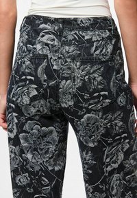 Crne traperice s sivim cvjetnim uzorkom, pet džepova i srednjim strukom, s detaljnim šavovima na leđima.