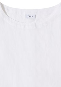 T-shirt blanc à col rond avec une petite étiquette rectangulaire en tissu sur laquelle est inscrit "CECIL" cousue à l'intérieur du col.