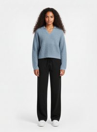 Světle modrý pletený svetr s výstřihem do V a límečkem, spárovaný s volnými černými kalhotami se stahovací šňůrkou v pase a bílými teniskami.