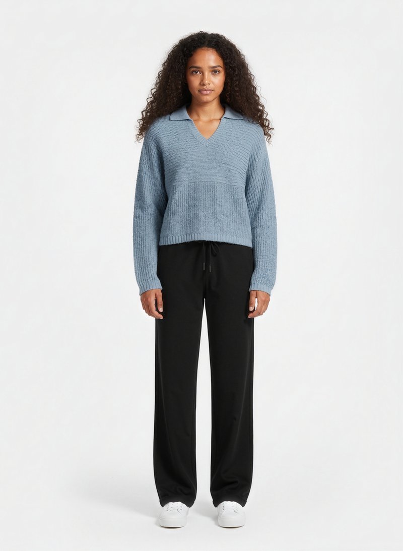 Světle modrý pletený svetr s výstřihem do V a límečkem, spárovaný s volnými černými kalhotami se stahovací šňůrkou v pase a bílými teniskami.