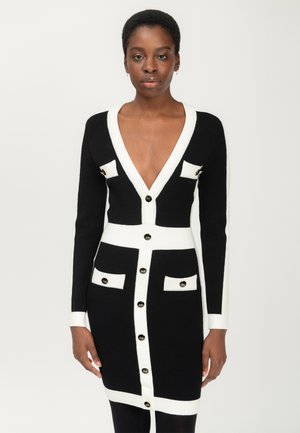 Vestido de punto con un profundo escote en V, bloques de color en blanco y negro, detalles en botones dorados y bolsillos en el pecho y caderas.