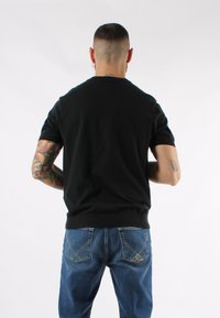 Maglione nero a maniche corte con scollatura rotonda, orlo aderente, abbinato a jeans in denim blu con cuciture a contrasto e dettagli sulle tasche.