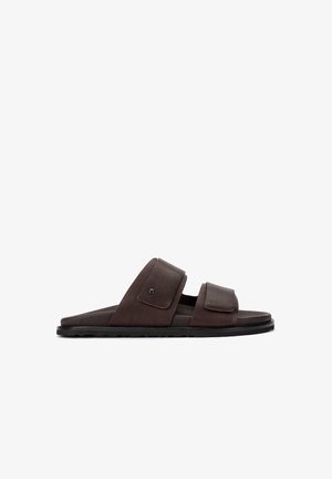 Sandale à enfiler en cuir marron avec deux brides réglables à Velcro et une semelle plate noire, vue de profil sur fond blanc.