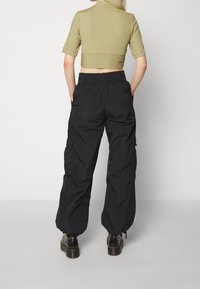 Zkrácený olivově zelený top s krátkými rukávy, spárovaný s volnými černými cargo kalhotami s elastickým pasem a bočními kapsami. Černé boty.
