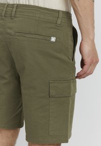 Shorts cargos vert olive à coupe droite, avec des poches latérales, une poche arrière et des coutures contrastantes le long des coutures.