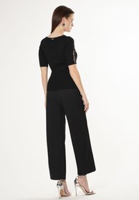 Top nero in maglia a maniche corte con bottoni decorativi, abbinato a pantaloni neri larghi e sandali con tacco alto in argento. Design semplice e aderente.