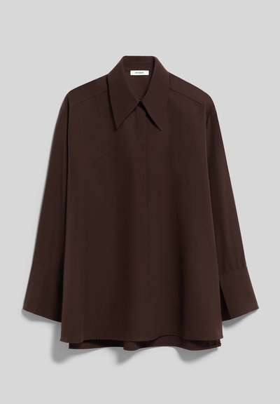 Chemise marron foncé à manches longues avec col large et pointu, boutons dissimulés sur le devant, et poignets repliés sur un fond gris clair.