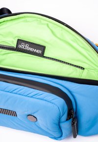 Pochette zippée bleue avec un intérieur en vert clair et une étiquette noire portant la mention "Clio Goldbrenner" à l'intérieur du compartiment principal.