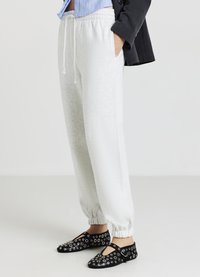 Pantalons de survêtement gris clair avec des poignets et une taille élastiques. Chaussures noires avec des découpes circulaires et des accents. Tenue décontractée avec une coupe ample.