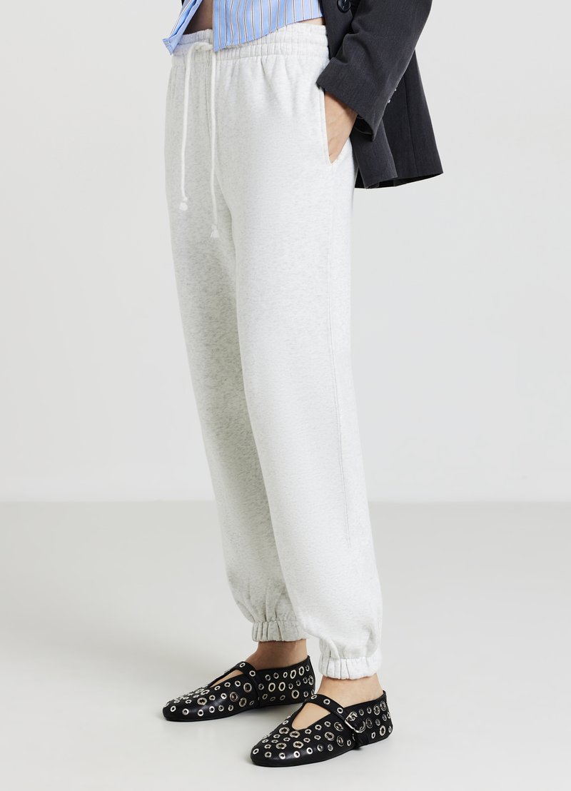 Pantalons de survêtement gris clair avec des poignets et une taille élastiques. Chaussures noires avec des découpes circulaires et des accents. Tenue décontractée avec une coupe ample.