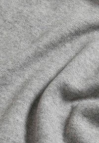 Szary dzianinowy materiał, prezentujący miękką teksturę z lekko melanżowym wzorem. Tkanina wykazuje gładkie fałdy i właściwości drapowania.