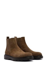 Botas Chelsea de ante marrón con paneles laterales elásticos, punta redondeada y suela de goma texturada. Incluyen lengüetas para facilitar el uso.