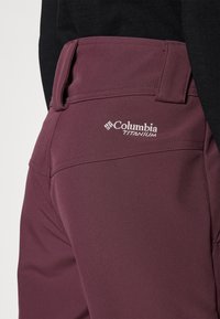 Viininpunaiset Columbia Titanium -housut, joissa on sileä kangaspinta, litteä vyötärö ja brodeerattu logo takataskussa.