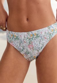 Kvetinový spodný diel bikín so zdobením na riasenie; má biely základ s viacfarebnými kvetmi, čo vytvára jemnú textúru a elastické prispôsobenie.