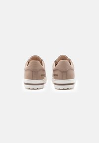 Ζευγάρι μπεζ αθλητικά Birkenstock, εμφανιζόμενα από πίσω, με λευκές σόλες με καφέ ρίγα και ορατό λογότυπο της μάρκας στους αστραγάλους.