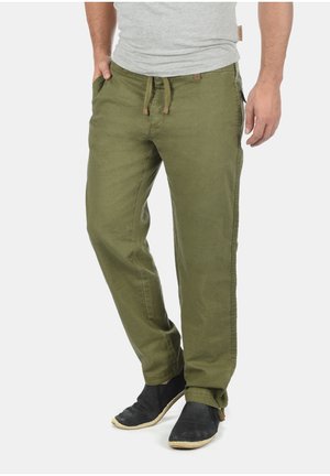 Olijfgroene, lichte broek met een ontspannen pasvorm, een koord in de taille, zijzakken en subtiele stiksels. Gecombineerd met zwarte instap schoenen.