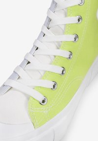 Leinenschuh mit weißem Grund und leuchtend limonengrüner Seitenfläche, weißen Schnürsenkeln, silbernen Ösen und strukturierter Oberfläche.