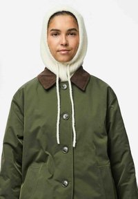 Veste imperméable verte avec un col en velours côtelé marron, dotée de grands boutons et d'une poche avant. Capuche tricotée blanche avec cordons de serrage.