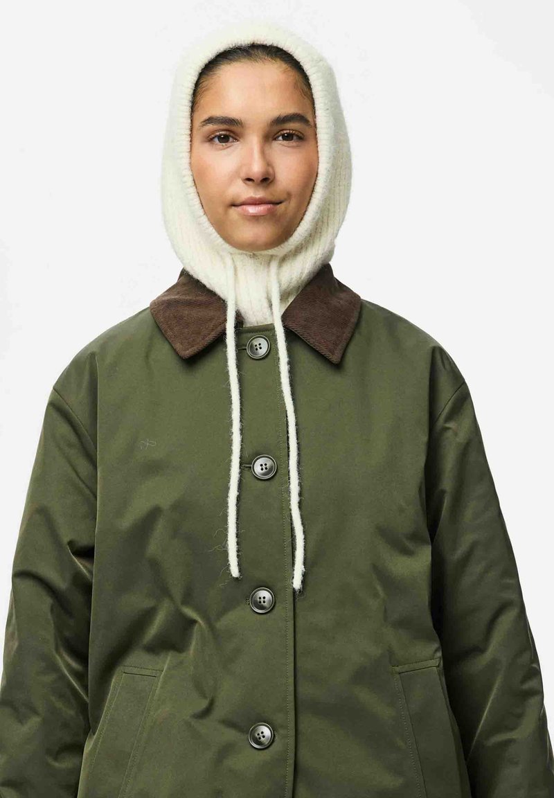 Veste imperméable verte avec un col en velours côtelé marron, dotée de grands boutons et d'une poche avant. Capuche tricotée blanche avec cordons de serrage.
