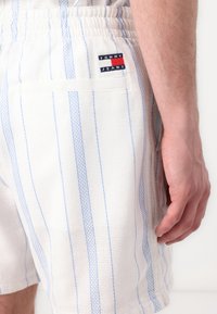 Hvide og lyseblå stribede shorts lavet af et struktureret stof. Har en elastisk talje og et lille logo-patch i sort, rød og blå.