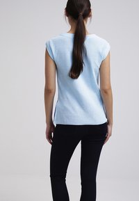 Světle modrý top bez rukávů s texturovanou tkaninou, kulatým výstřihem a kontrastními tmavými bočními panely, kombinovaný s tmavými džíny.