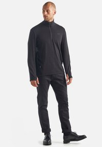 Sort langærmet pullover med kvart-zip krave, tekstureret stof og tætsiddende design, parret med sorte bukser med rullebund og sorte støvler.