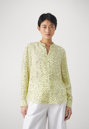 Gul langermet bluse med et teksturert mønster av svarte squigglier, med en liten krage og en knappelukking foran.