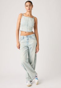 Φωτεινό cropped τοπ από τζιν με ρυθμιζόμενες τιράντες, συνδυασμένο με τζιν ίσιας γραμμής. Λευκά αθλητικά παπούτσια με μπλε και κόκκινες λεπτομέρειες ολοκληρώνουν το σύνολο.