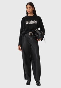 Musta pörröinen neule, jossa edessä teksti "Saints", yhdistetty mustiin leveälahkeisiin nahkahousuihin ja mustiin korkokengällisiin nilkkureihin.