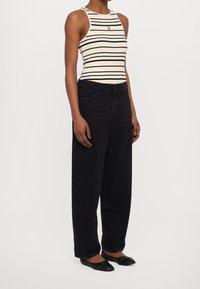 Top sin mangas ajustado a rayas en crema y negro, combinado con jeans de mezclilla negros de tiro alto y corte holgado, y zapatos de ballet.