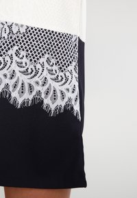 Černá sukně s bílým krajkovým lemem na spodním okraji, s texturovanou látkou nahoře, která zahrnuje vzorovanou pletenou část a hladké části.